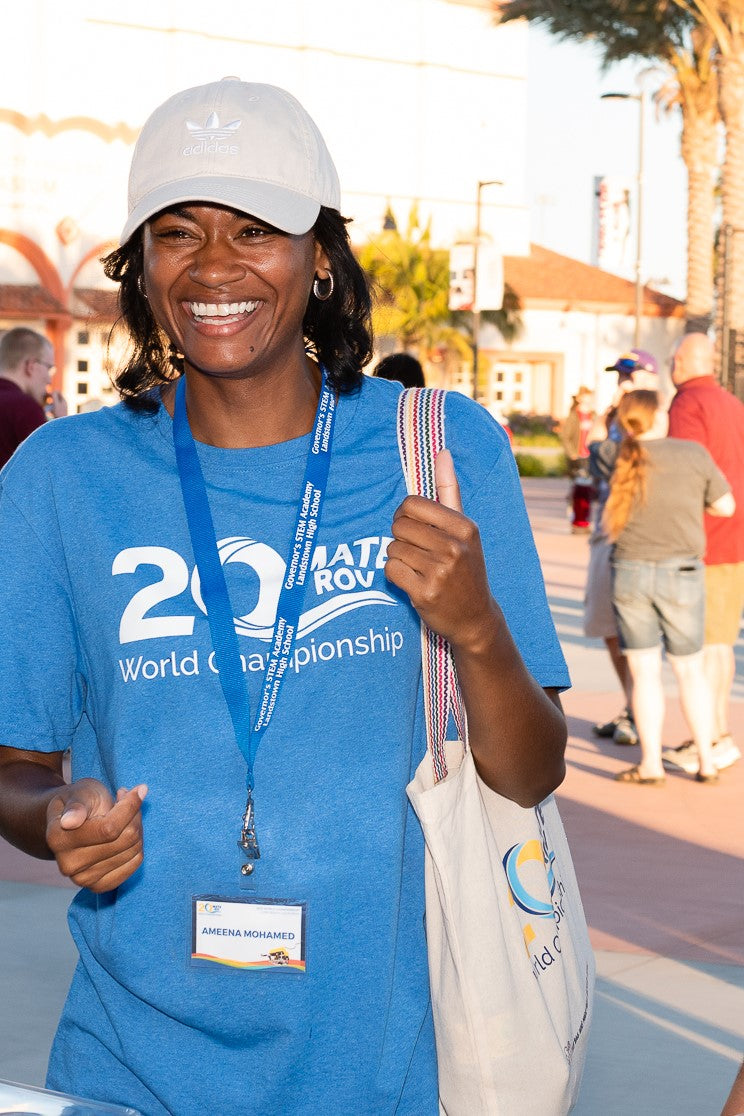 Woman wearing a blue MATE 20th Anniversary Tee Shirt and carrying a matching canvas tote bag