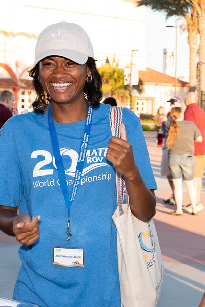 Woman wearing a blue MATE 20th Anniversary Tee Shirt and carrying a matching canvas tote bag